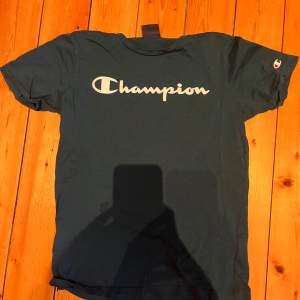 Säljer en snygg mörkblå t-shirt från Champion i storlek L. Den har en klassisk Champion-logga i vitt på bröstet och en liten logga på ärmen. Perfekt för vardagsbruk eller träning. T-shirten är i bra skick och superbekväm!