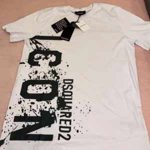 Dsquared2 T-shirt  - Säljer en snygg vit t-shirt från Dsquared2 i nyskick. Den har ett coolt svart tryck med texten 'ICON' och märkesnamnet på framsidan. Perfekt för en avslappnad stil eller att bära på fest. T-shirten är kortärmad och gjord i mjuk bomull. Passar perfekt till jeans eller shorts! Den är helt oanvänd!