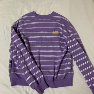 Lila långärmad tröja  - Lila/vit/svart randig sweatshirt från Junkyard. Tröjan har ett gult tryck på vänster sida. Tröjan är använd men är i fint skick! Du betalar priset (250kr)+frakt. 