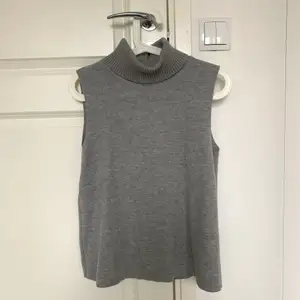 En grå armlös polotröja med stickad krage. Inga sömmar och blir varken stickig eller nopprig. Jättesnygg som den är eller med en skjorta, t-shirt eller tröja under. I nyskick!