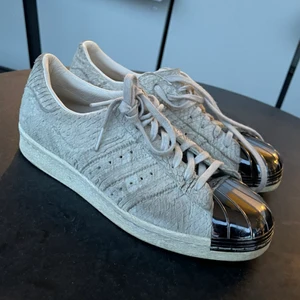 Adidas Superstar storlek 38 - Beige/grå Adidas Superstar i ”ormskinn” med stålhätta längst fram. Unik och cool modell – har älskat dem! De är i använt skick, men har inga slitningar eller defekter. Storlek 38.