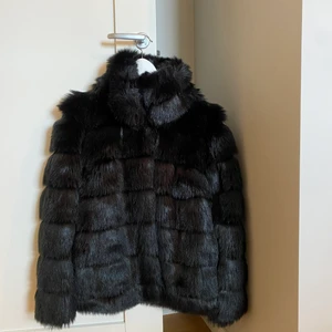 Svart pälsjacka - En snygg svart pälsjacka från Nelly. Den är riktigt varm och perfekt för vintern. Använd ett fåtal gånger.