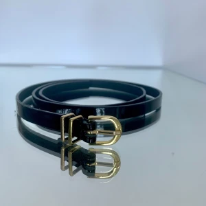 Smalt skärp i läder/ stl: 85 - Bälte i blankt läder med guldfärgat spänne. Storlek 85. Fint använt skick. Höjd: 1,2 cm.