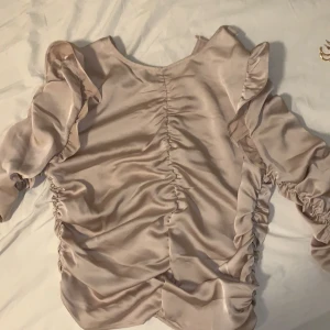 Helt ny superfin festlig blus - Aldrig använd. Brudrosa/ nude/roséguld aktig. Från h&m köpt för 199. Detaljerad med volanger & fint mönster. Liknande silkesmaterial. Aldrig fått tillfälle att använda den & därför säljer jag den. Storlek S