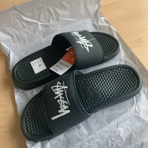 Nike Benassi Stussy Off Noir Size 9 (42,5 EU) - Nike Benassi Stussy Tofflor fabriks nya tofflor oanvända. Vunna på en raffel från Nike Snkrs. Storlek 42,5 EU. Kontakta mig för fler bilder!