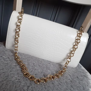 Vit väska  - Superfin vit crocmönstrad väska med guldkedja som handtag. Från Nly men slutsåld där(Nypris:349kr). Fint skick då endast använd en gång. Frakt: 66:- Spårbart💓