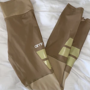 brun/ beiga aimn tights  - Säljer mina älskade brun/beiga träningstights från aimn! Tightsen har olika beiga detaljer och en bekväm hög midja!!🥳 vid flera intresserade vinner högsta bud!