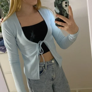 Ljusblå ribbad kofta  - Koftan har band i mitten som går attt knyta upp, den är ribbad, tajt längs armarna, stretchig. Mått axlarna: 37cm mått mitten 50cm. Helt oanvänd 