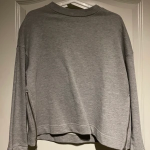 Grå sweatshirt - Grå sweatshirt med dragkedja bak i nacken samt på båda sidorna. Köpt på Ullared. Köparen står själv för frakten.
