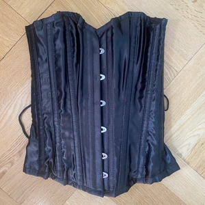 Korsett - Svart korsett med snörning. Passar S, står storlek 22 i.