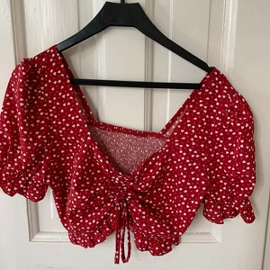 Röd topp  - Söt röd topp med hjärt-mönster. Knytning fram, så kan själv bestämma hur kort den ska vara. Aldrig använd, storlek 38/M