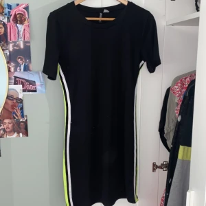 Svart klänning  - Svart klänning med vit och neon grön/gula ränder på sidan. Säljer pga för stor. Köparen står för frakten :)