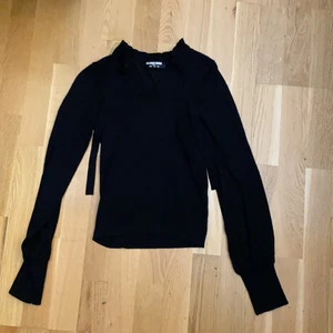 svart blus, storlek 36 - svart tröja med skön material. Ribbat material vid handledarna men även nere vid tröjan. Lite mönster över brösten och runt halsen är det ribbat material fast med volanger. Du kan välja hur hård krage du vill ha genom snören som finns vid halsen. Aldrig använd.