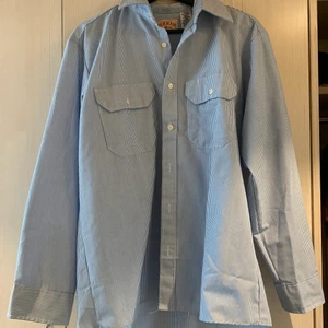 Snygg skjorta i bra material  - Randig skjorta i ganska ”hårt” material som gör att den sitter snyggt. Oversize modell i bomull och polyester. Storlek L men sitter bra på mig som är storlek M. Köpt vintage, tillverkad i Honduras. 