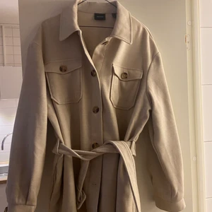 Beige kappa  - Säljer denna fina beiga kappa från Vero Moda med bruna knappar och knyte i midjan. Storlek L men passar bra till mig som är S/M eftersom man kan knyta åt i midjan!😇