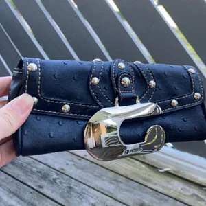 Guess väska  - Liten söt plånboksväska från Guess.  Längd 20 cm höjd 9cm. Repa på spännet. Saknar rem att hålla i men fin att bara ha som clutch, därav lågt pris. Frakt tillkommer 60kr