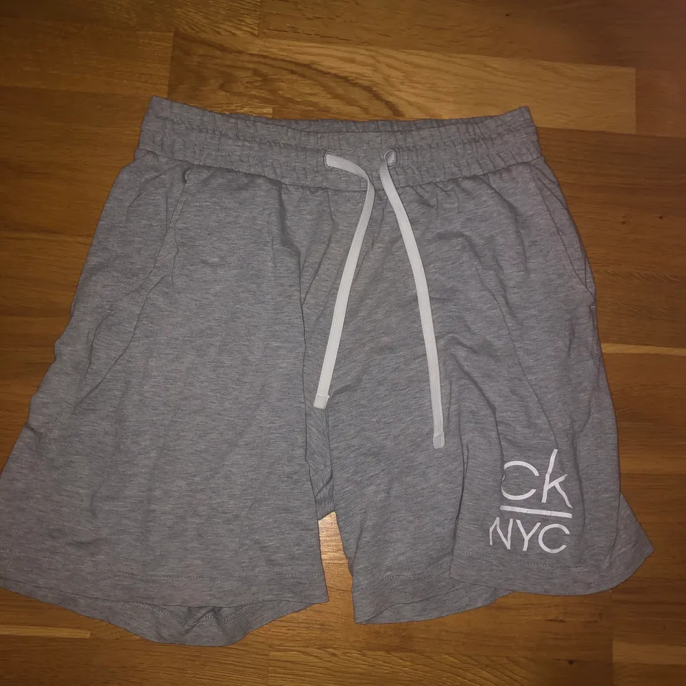 Ett par gråa Calvin Klein shorts i storlek S med en ”CK NYC” logga på benet och en mindre sådan på bakfickan. Dessa är perfekta under sommaren då de är tunna men kan användas som sköna och snygga shorts att ha hemma också. Köptes för 600kr på Volt i Uppsala men säljer för bara 100kr! . Shorts.