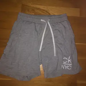 Ett par gråa Calvin Klein shorts i storlek S med en ”CK NYC” logga på benet och en mindre sådan på bakfickan. Dessa är perfekta under sommaren då de är tunna men kan användas som sköna och snygga shorts att ha hemma också. Köptes för 600kr på Volt i Uppsala men säljer för bara 100kr! 