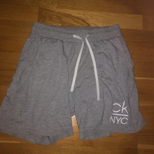 Calvin Klein shorts  - Ett par gråa Calvin Klein shorts i storlek S med en ”CK NYC” logga på benet och en mindre sådan på bakfickan. Dessa är perfekta under sommaren då de är tunna men kan användas som sköna och snygga shorts att ha hemma också. Köptes för 600kr på Volt i Uppsala men säljer för bara 100kr! 