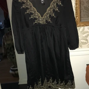 Svart klänning - Svart kort klänning med knytning i midjan. Superfin med guldiga ditaljer runt v-ringning och längst ner. I fint skick✨ köparen står för frakt 