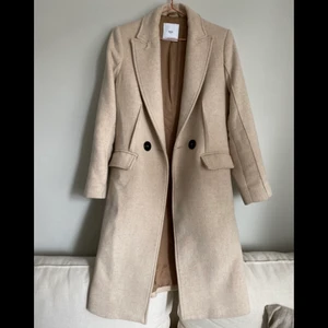 Beige kappa - Så fin beige kappa i ullblandat material, varm och skön alltså! Knappt använd, sprucken söm inne i ena fickan som jag lagat🥰 annars toppenskick! Går strax under knäet på mig som är 165cm Nypris ca 1800kr