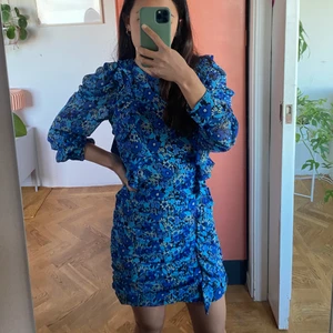 Blommig klänning från Zara - Fin blå blommig mini klänning från Zara. Den är öppen på baksidan och har puffärmar. Använd bara en gång i julas, så den är i perfekt skick!