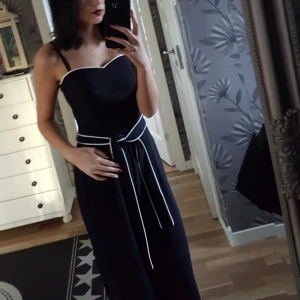 Svart jumsuit - Svart jumsuit köpt 2018 använda 2 ggr, nyskick. Axelbanden går att ta av, dragkjedja på sidan