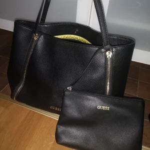 Guess väska  - En fin guess väska knappt använd, följer med en liten som man kan ha inuti eller bara som den är. Svart med guld detaljer, bra vardags storlek. 