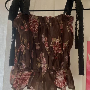 Topp - Så fin blommig topp i mörkt brun! Går att knyta banden som man vill ha de eller som en tub topp. Helt ny med lappar kvar!!