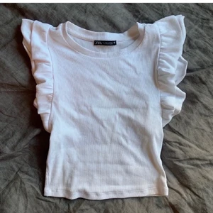Vit topp med volang - Jättesöt vit topp från Zara! Säljer för att jag inte använder längre💓💓 En pytteliten fläck som inte går bort i tvätten dock, skriv om jag ska skicka bild! BUDGIVNING PÅGAR TILL MÅNDAG 21/2 16:00 ISTÄLLET!