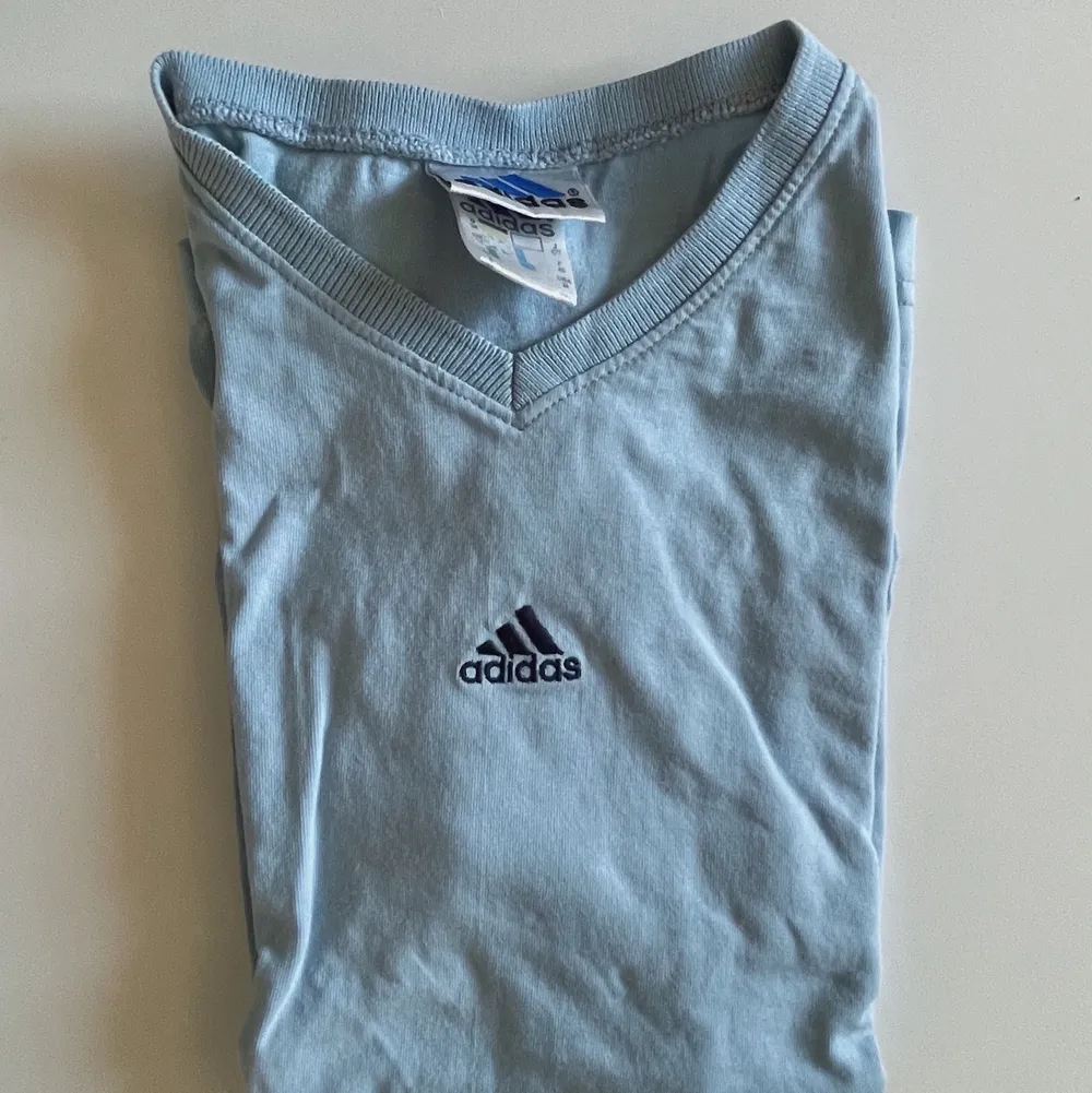 En ljusblå v ringad T-shirt från Adidas. Den har ett jättelitet hål längst ner på tröjan som knappt syns. Vintage!. T-shirts.