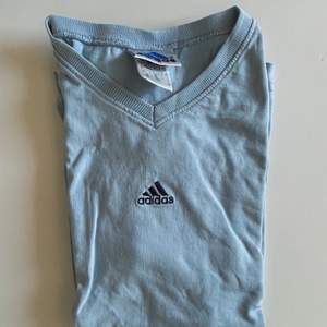 En ljusblå v ringad T-shirt från Adidas. Den har ett jättelitet hål längst ner på tröjan som knappt syns. Vintage!