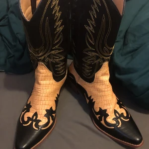 Cowboy boots i nyskick (strl 45-46) - Cowboy boots i läder . Svarta och beige/gula fina detaljer i brodyr. Nyskick! Kan även skickas i vanlig påse (45kr) . Köparen både väljer och betalar frakt.