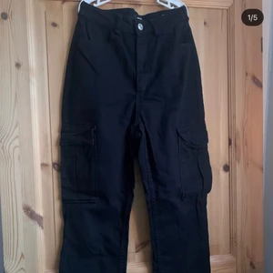 Svarta cargo byxor - Detta är ett par svarta cargo jeans som jag själv tycker är väldigt coola. Har använt dom en gång så de är i väldigt gott skick🤍 Byxorna har fickor på sidorna, en knapp på varje höger och vänster sida vid midjan, och ser ganska små ut i slutet av byxorna men är väldigt stretchiga.  Byxorna är från BikBok🤍
