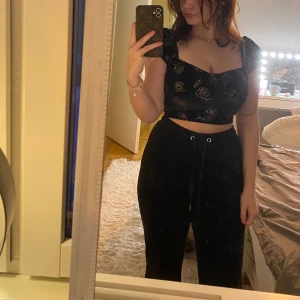 Topp i svart med guldiga rosor - Säljer en jättefin svart satin topp med guldiga rosor. Jättegulliga ärmar. Behöver tyvärr sälja den då den blir för liten över bysten. Från Motel i storlek XS.