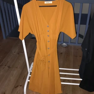 Lång orange klänning med knappar - Knappt använd, i bra skick , tajt runt midjan 