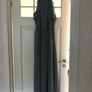 Klänning  - Jag säljer nu en superfin sommar/ bal klänning som är oanvänd, då den inte passade mig. Klänningen är en långklänning i en blågrå färg med dragkedja i ryggen och volanger i ärmarna. 