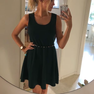 Mörkgrön klänning (inkl skärp) - Mörkgrön klänning med svart skräp. Tjockare tyg, perfekt för lite kallare väder. Inköpt i London. Material: 79% Polyester, 17% Viskos, 4% Elestan.