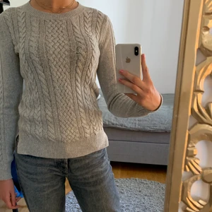 Tröja - Grå tröja som har kabelstickat mönster på framsidan och slitsar på sidorna.