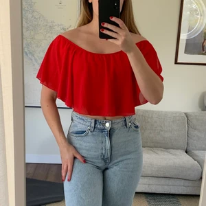 Röd topp/blus - Jättefin topp/blus som man kan anpassa lite själv med resår runt axlarna så man kan ändra om man vill ha u-urringning eller att den går över axlarna som på bilden. Finns ett tyg under volangerna som man kan vika upp beroende på hur mycket man vill visa av magen. Stretchigt och skönt tyg, storlek skulle jag säga är XS-M 🥰. Har en till i svart!