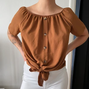 Topp med knappar och knytdetalj strl S-L - Brun topp, färgen är rättvis på bild 1, står storlek L men passar även mindre storlekar. Resår i urringningen så går även att dra ned ärmarna över axlarna och använda den som ”off-shoulder”