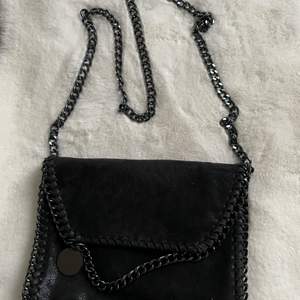 En svart väska med svart kedja som axelband! Insidan har 3 fickor en med dragkedja. Använt kanske 3ggr! Fint skick!