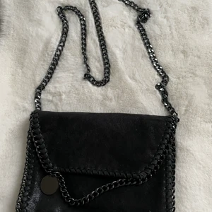 Svart axelväska  - En svart väska med svart kedja som axelband! Insidan har 3 fickor en med dragkedja. Använt kanske 3ggr! Fint skick!