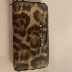 Michael Kors plånbok  - En Micheal Kors plånbok, köpt för några år sen. Har slitits bort lite ”päls” så den är inte ”hårig” längre men mönstret är fortfarande lika fint. Även lite sliten på en av bokstäverna men det syns på bilden. Köpt för ca 1500kr Säljpris går att förhandla!