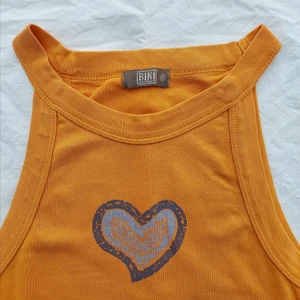 Linne med hjärta - Ett linne I orange färg med lila hjärta. Passar mig som är S men kan nog passa både XS och M med. Är uppvikt på sista bilden