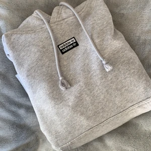 Adidas hoodie  - Säljer denna fina adidas hoodie i fint skick! Hoodien är ljusgrå och har adidas märket längst fram. Hoodien har även adidas-detaljer på ärmmuddarna och har en stor och mysig luva. Frakt tillkommer💗