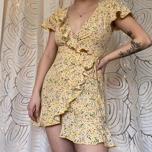 Somrig gul omlottklänning med volanger - Superfin sommarklänning från shein. Använd en gång och säljer då den är lite för urringad för min smak. På bilden ser den ut att vara olika lång på sidorna men det är bara på grund av min pose. Vid stort intresse får ni buda privat💞
