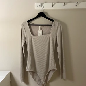 Body från H&M - En body i beige-grå från H&M! Oanvänd, & därav i fint skick 😍 Frakt tillkommer.