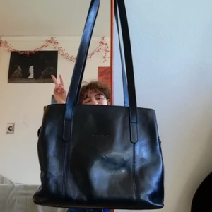 Svart handväska i skinn - Svart handväska i skinn från luca ferri, inhandlad second hand. Tre stora fack har den, som alla öppnas/stängs med dragkedja. Mittenfacket har två små fickor med dragkedja i. Ca 25cm i bredd X 22cm i höjd och 7cm i djup. 