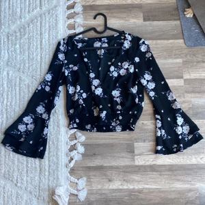 Svart urringad blus med blom-tryck - En super fin sommar/vår tröja med vita blommor. Den är urringad, tyget korsar sig vid urringningen. 